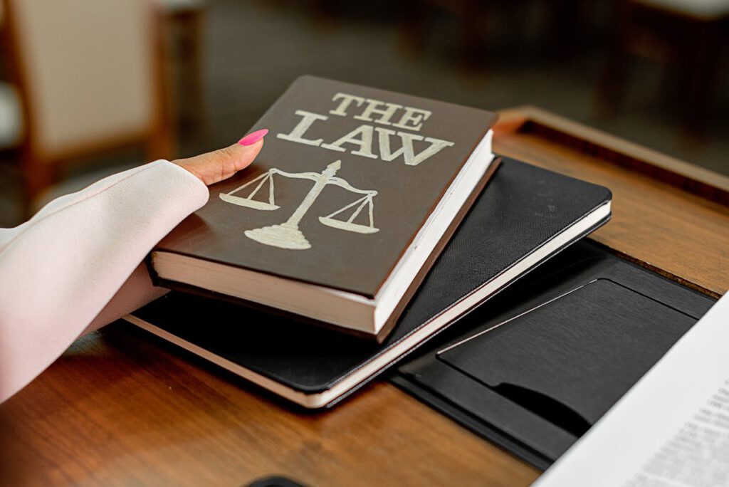 Closeup image of a law book titled The Law on a wooden desk with scales of justice.